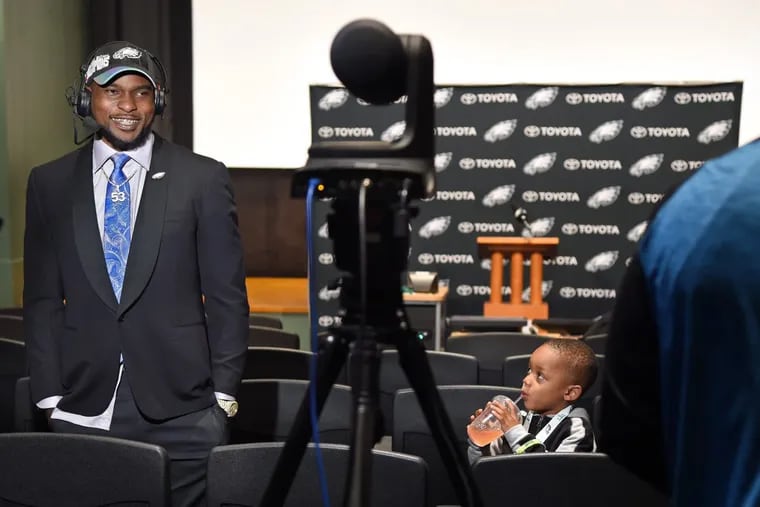 With his 3-year-old son Nazir (right) looking on, Eagles linebacker Nigel Bradham gives a TV interview Thursday.
