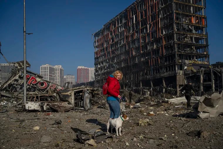 Irina Zubchenko walks with her dog Max amid the destruction caused after shelling of a shopping center, in Kyiv, Ukraine, Monday, March 21, 2022. The World Bank said Sunday, April 10, 2022 that Ukraine's economy will shrink by 45.1% this year because of Russia's invasion, which has shut down half of the country's businesses, choked off imports and exports and damaged a vast amount of critical infrastructure. (AP Photo/Rodrigo Abd, File)