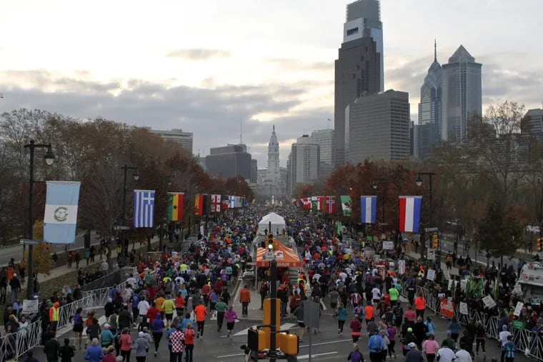 Runners make their way down Benjamin Franklin Parkway during the Philadelphia Marathon. Onlookers with signs are cheering them on.