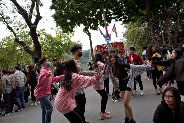 Youth dance in a street as flags of North Korea and the U.S are flown in Hanoi, Vietnam, Sunday, Feb. 24, 2019. The second summit between U.S President Donald Trump and North Korean leader Kim Jong Un will take place in Hanoi on Feb. 27 and 28. (AP Photo/Gemunu Amarasinghe)