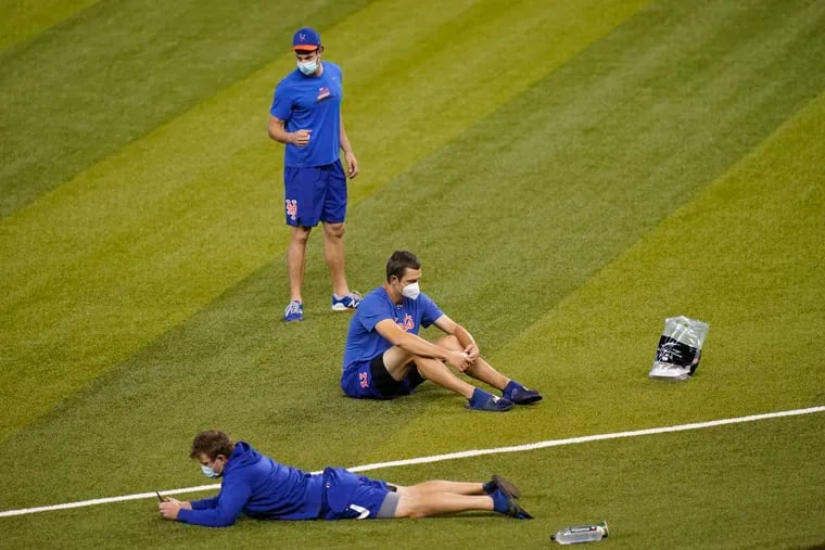New York Mets players sit on the field before a baseball game against the Marlins Thursday in Miami. Major League Baseball says the Mets have received two positive tests for COVID-19 in their organization, prompting the postponement of two games against the Marlins.