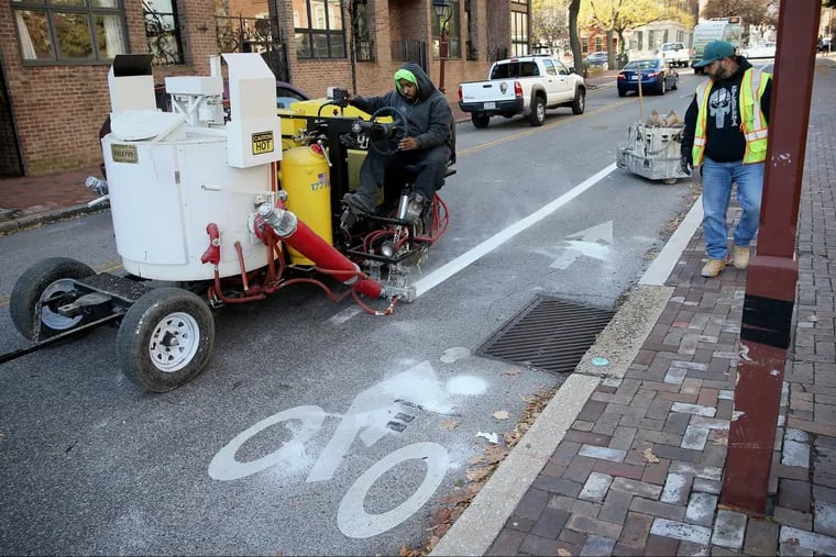 Darryl Carroll (left), a Philadelphia Streets Department line striper crew chief, repaints a bicycle lane line on Spruce Street as fellow worker Jose Gonzalez follows his progress. The restriping in December, which was previously scheduled, took place days after a bicyclist was killed in a crash at 11th and Spruce Streets.