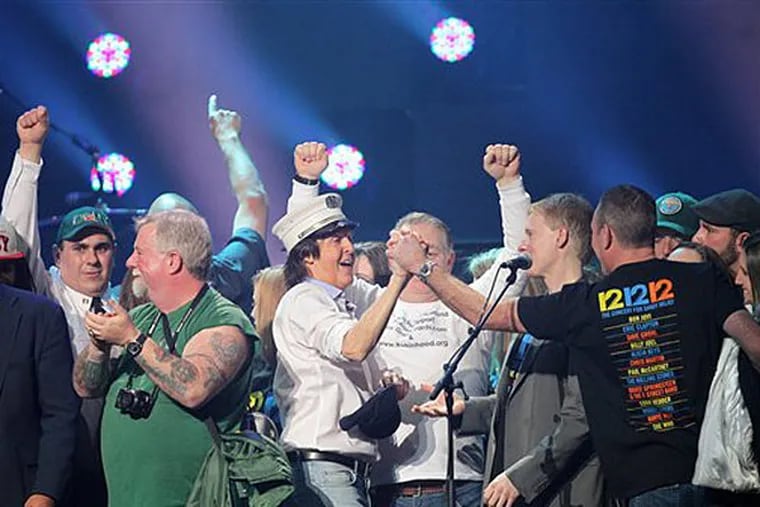 This image released by Starpix shows Paul McCartney, center, on stage with firefighters at the 12-12-12 The Concert for Sandy Relief at Madison Square Garden in New York on Wednesday, Dec. 12, 2012. Proceeds from the show will be distributed through the Robin Hood Foundation. (AP Photo/Starpix, Dave Allocca)