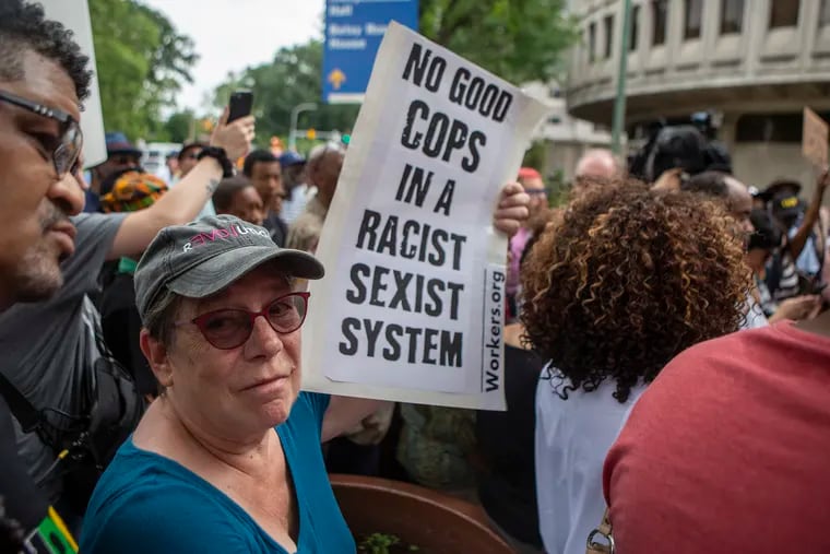 Betsey Piette, 70, of West Philly, holds up a sign as a crowd of people gather outside Philadelphia Police headquarters at 8th and Race streets to protest the 330 active Philadelphia police officers included in a database of racist Facebook comments on Friday, June 07, 2019.