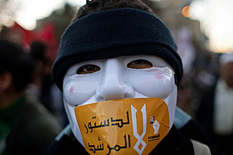 An Egyptian protester with a mask on his face and a sticker with Arabic that reads "No for the constitution of the Morshid," during an anti-president Mohammed Morsi protest near the presidential palace, in Cairo on Friday. Egypt's political crisis spiraled deeper into bitterness and recrimination Friday as thousands of Islamist backers of the president vowed vengeance at a funeral for men killed in bloody clashes earlier this week and large crowds of the president's opponents marched on his palace to increase pressure after he rejected their demands. NASSER NASSER / Associated Press