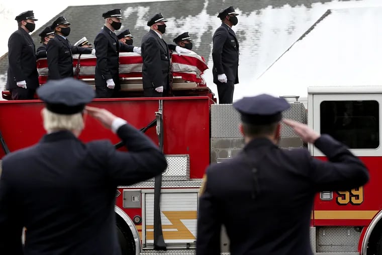 Philadelphia firefighters salute during the funeral procession as the casket of John Evans passes.