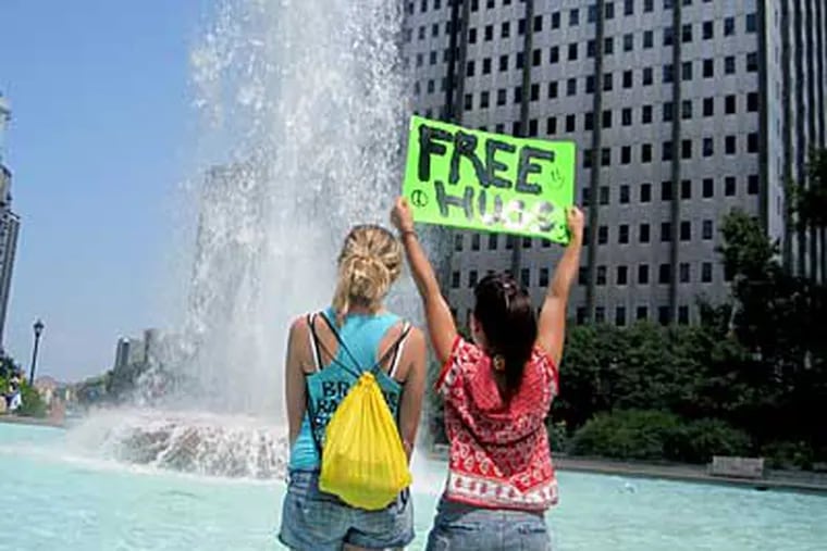Lilyana Cao (right) and Brittany Pesta with a sign offering Free Hugs, cool off in the Love Park fountain. (Litty Samuel/Staff)