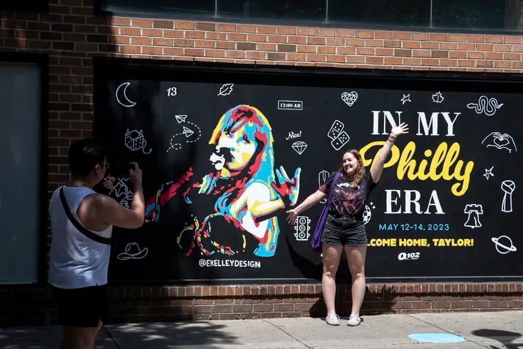 (left) Christian Perucho, of Graduate Hospital, takes a photo of Alyssa Campbell posing at the Taylor Swift mural by Emily Kelley near 2nd and South Streets in Philadelphia, Pa. on Wednesday, May 10, 2023. Taylor Swift performs in Philly this weekend.