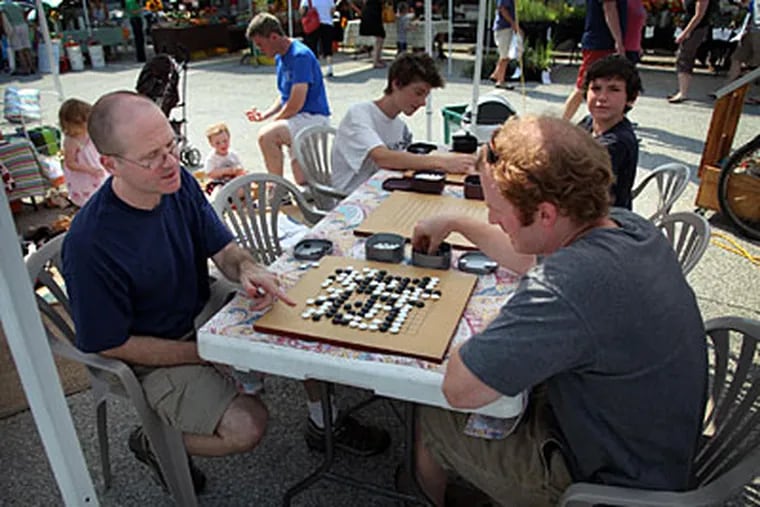 At the Phoenixville Farmers' Market, Craig Brown (left) squares off against Dane Percy. "It's a really weird feeling," Brown says of the game. "It feels meditative, and yet it feels very competitive at the exact same time. There's nothing for me that does that other than go." (LAURENCE KESTERSON / Staff Photographer)