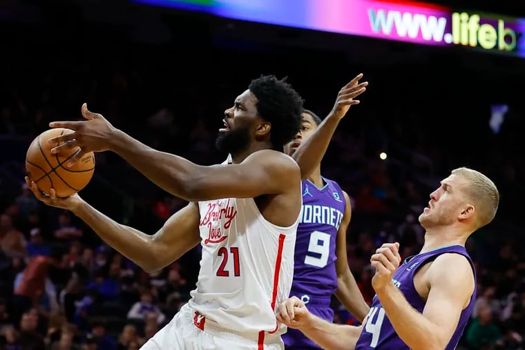 Sixers center Joel Embiid grabs the basketball past Charlotte Hornets guard Theo Maledon and center Mason Plumlee in the second quarter on Sunday, December 11, 2022 in Philadelphia.
