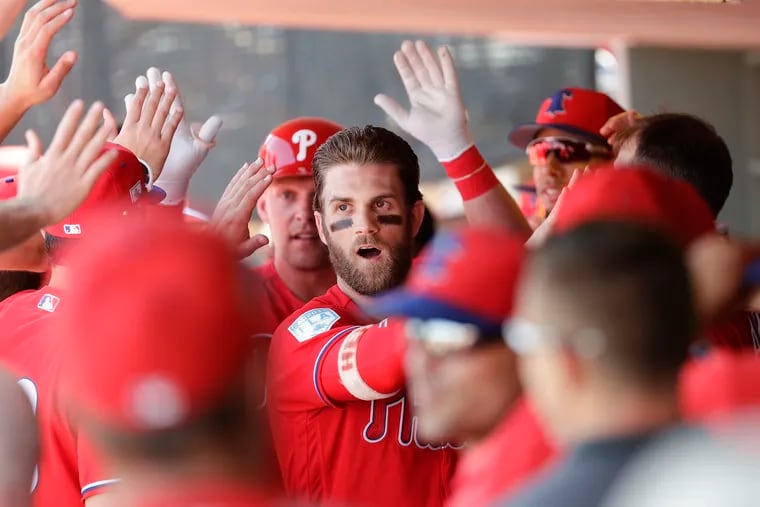 Bryce Harper high-fives teammates after Rhys Hoskins batted him home with a two-run home run in Saturday's spring-training game.