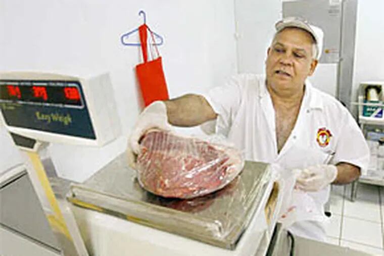 A hefty steak, perhaps to become the centerpiece of a Brazilian churrasco, is weighed by Adeladio Rodrigues at the Bull Boi market on Castor Avenue. (Elizabeth Robertson / Staff Photographer)