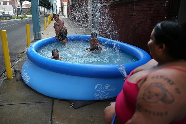 Maria Schermety, left, sprays her grandchildren with water as they play in a pool on the sidewalk along Front Street near Cecil B. Moore Avenue in Philadelphia on July 20, 2015. The children are lIsaiah Pizarro, 3, left, Zahamir Burch, 9, center, and Isaac Adorno, 6, right.  ( DAVID MAIALETTI / Staff Photographer )
