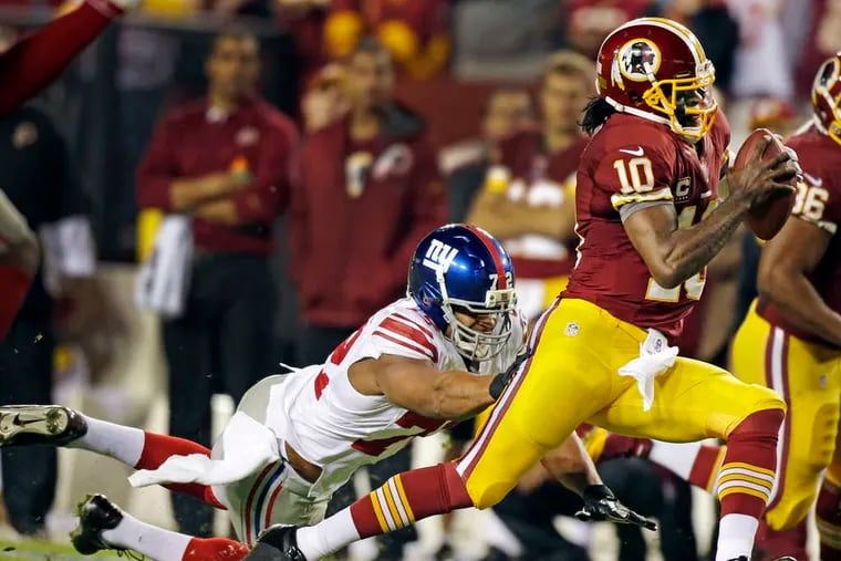 Redskins quarterback Robert Griffin III tries to escape the grasp of the Giants' Osi Umenyiora. New York led, 13-10, in the third quarter of Monday night's game, which ended too late for this edition.