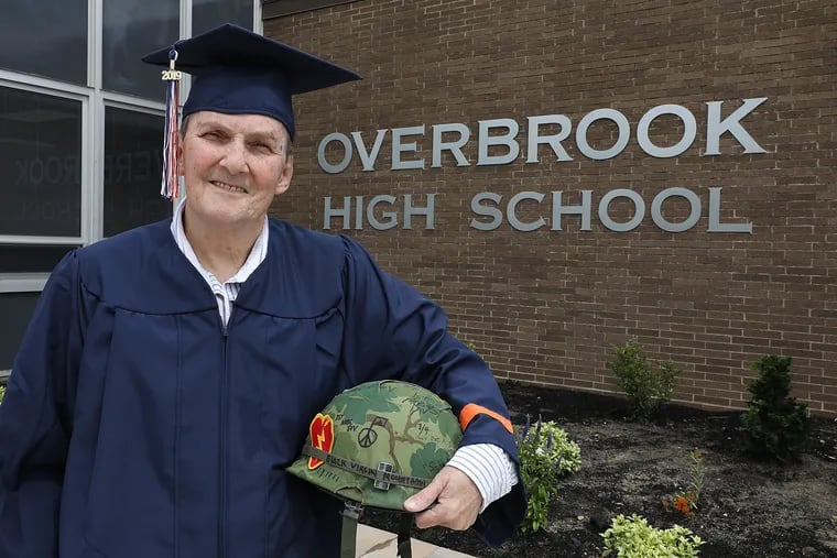 George Schaefer Jr. stands outside Overbrook High School holding his Vietnam war helmet. He dropped out to join the Army and will receive his diploma 50 years later.