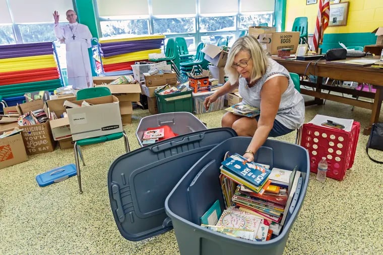 With a cardboard cutout of Pope Frances, looking on, Peggy Mack, a volunteer mom, helps sort through the children's books that were donated to the students of Our Lady of Angels Schools in a classroom at Cardinal O'Hara High School. OLA was destroyed by fire in July, and a contingent of parents and community members are helping the elementary school's students prepare for the school year inside the high school.