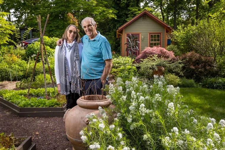 Marilyn Sifford and Bob Butera within the vegetable garden with a wind sculpture and the potting shed in background. The gardens are landscaped with wood chip paths.