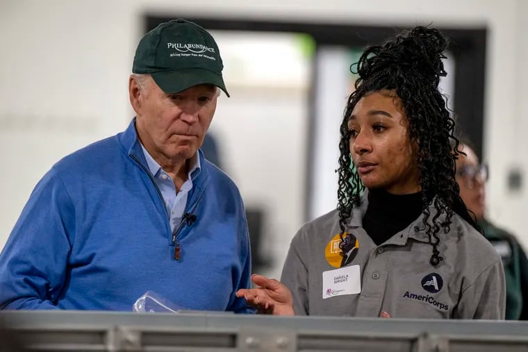President Joe Biden talks with Dañiela Wright as he bags fruit into boxes on a conveyor belt in the packing room while volunteering at Philabundance on Martin Luther King Jr. Day on Monday.