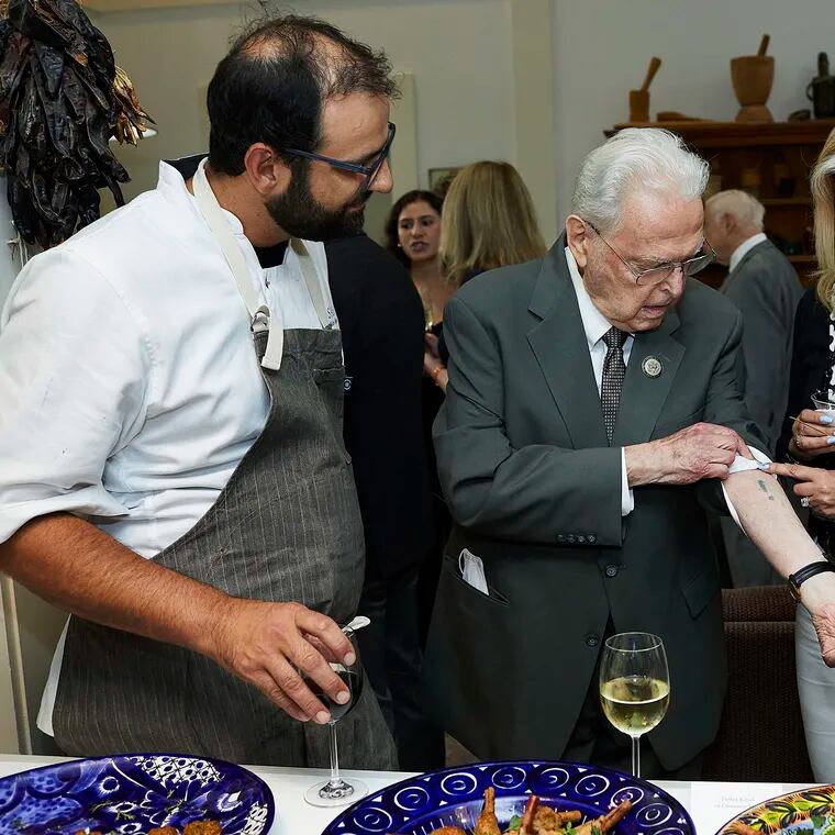 Holocaust survivor Steven Fenves, with chef Alon Shaya (left), shows a prisoner number tattooed on his arm at Auschwitz to guests at a June 2022 fundraising dinner for the United States Holocaust Memorial Museum in Washington, D.C.