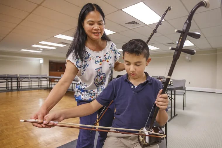 Qin Qian, an erhu player and teacher, left, guides the bow hand of Jordan Paynter, 11, right, as he participates in his fourth lesson with Qin Qian on August 29, 2018.