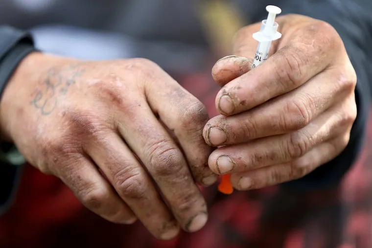 Robert Hilton holds on to a needle after using heroin along the railroad track in Kensington in Philadelphia, PA on October 25, 2017.  DAVID MAIALETTI / Staff Photographer