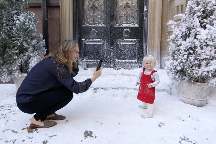 Paulina Seczak of Phila. takes photographs of her 16 1/2 month old daughter Ella Seczak in the fake snow on the 2100 block of Spruce St. in Phila., Pa. on Oct. 22, 2020. The two were out for a walk when they discovered the snowy scene and it was just good luck that Ella was already wearing a red dress. Servant, the creepy nanny show Chester County-based filmmaker M. Night Shyamalan is producing for Apple TV, is currently shooting on and around the 2100 block of Spruce St. and when the crew is not actively shooting folks are allowed to enjoy the scene as they pass thru the neighborhood.