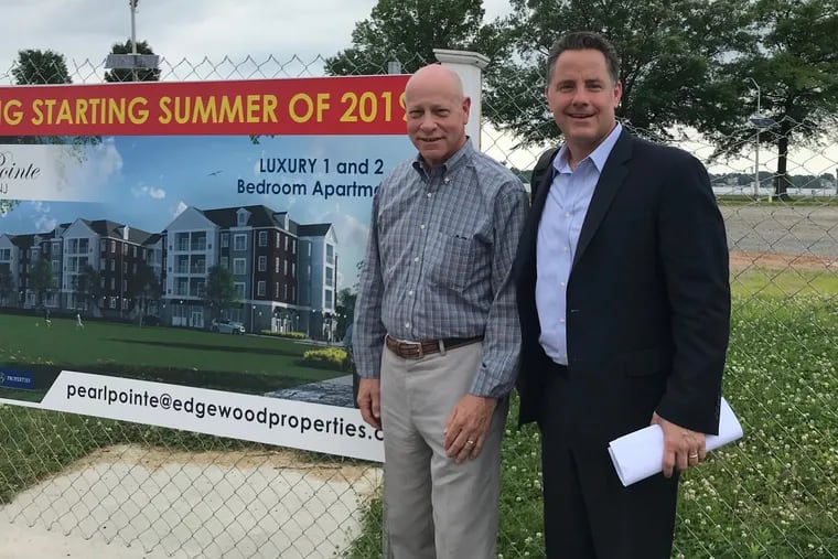 Jim Kennedy (left) and John Callahan, who are working on the redevelopment of Burlington City, stand by the sign that announces a new luxury apartment complex that will be built in a parking lot along the Delaware River.