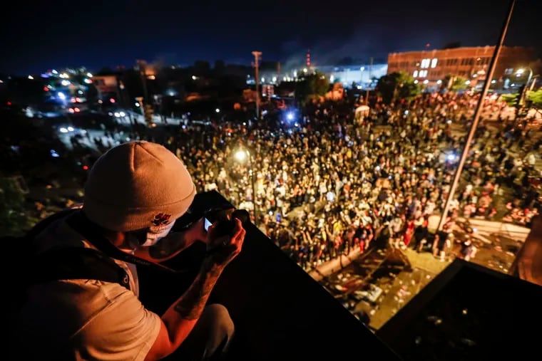 A protestor takes a picture of a demonstration from the roof of the Minneapolis 3rd Police Precinct, Thursday, May 28, 2020, in Minneapolis. Protests over the death of George Floyd, a black man who died in police custody Monday, broke out in Minneapolis for a third straight night.