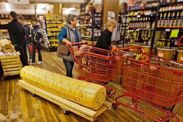 Shoppers at Bagliani's Market maneuver around a 700-pound torpedo of sharp provolone, one of four delivered in late summer and aged in the store until early December, when hundreds of people gather to see the first one cut. (David M Warren/Staff)