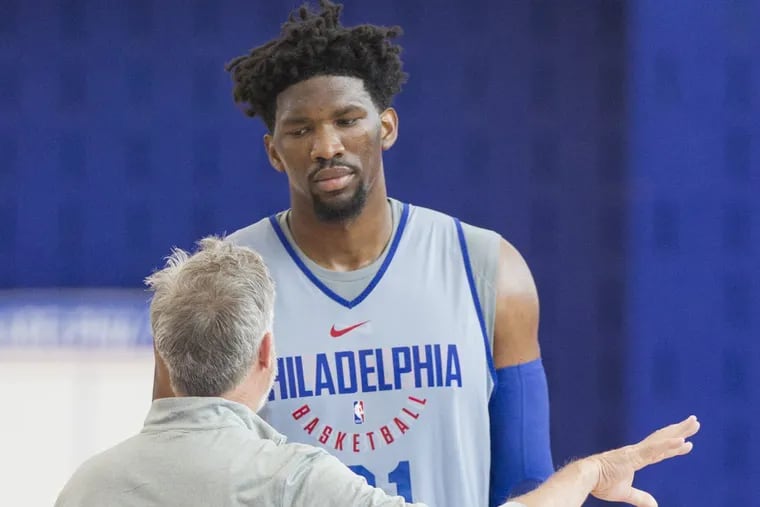Joel Embiid talks to coach Brett Bown on the first day of practice last month.