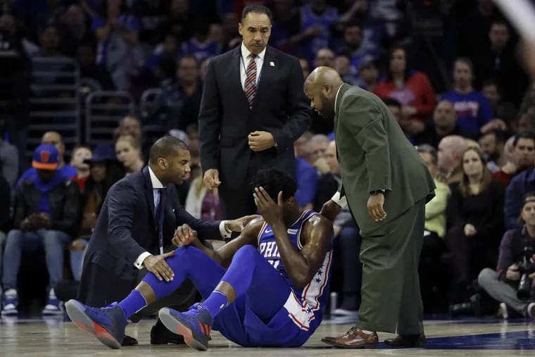 Joel Embiid, center, lies on the court after an injury during the first half of an NBA game against the New York Knicks Wednesday.