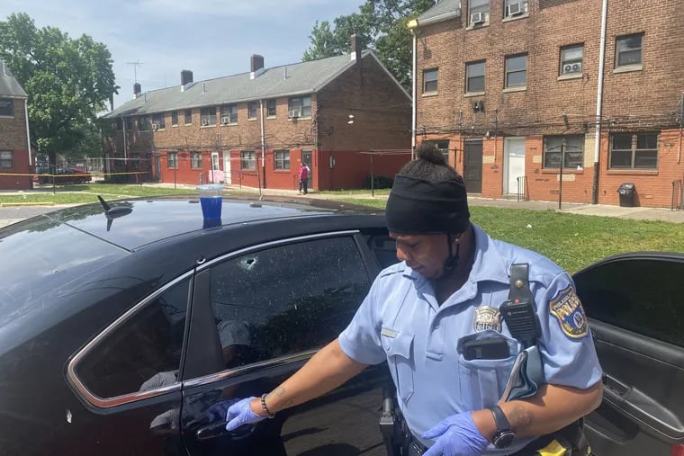 A Philadelphia police officer inspects a car with a bullet hole in the rear passenger side window in the 600 block of Franklin Place. Seven people were shot on the block just after midnight Wednesday. One victim died.