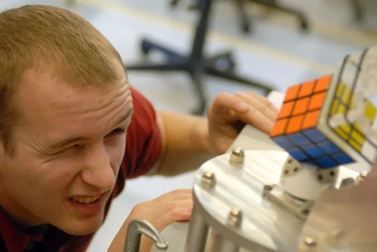Electrical and computer engineering major Zach Grady positions a cube on the Rubik's Cube-Solving Robot he helped create at Rowan University. (Tom Gralish / Staff Photographer)