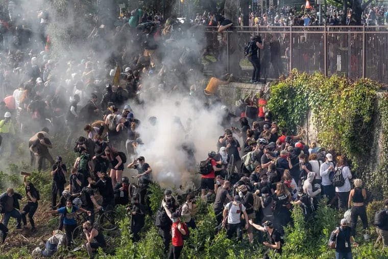 Protesters scramble from the Vine Street Expressway after tear gas is fired to clear them from blocking traffic on the major east-west thoroughfare on Monday, the third day of confrontations over the police killing of George Floyd in Minneapolis.