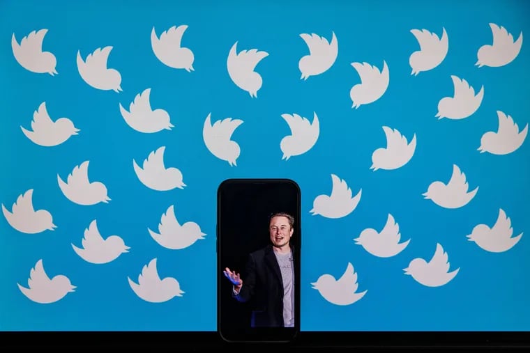 A cellphone displaying a photo of Elon Musk placed on a computer monitor filled with Twitter logos in Washington, D.C.