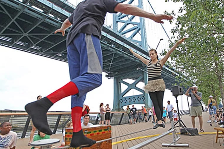David Gillies (left) and Erica Saben work on their wire act as the Give and Take Jugglers get warmed up before their performance at The Race Street Pier. ( Michael Bryant / Staff Photographer )