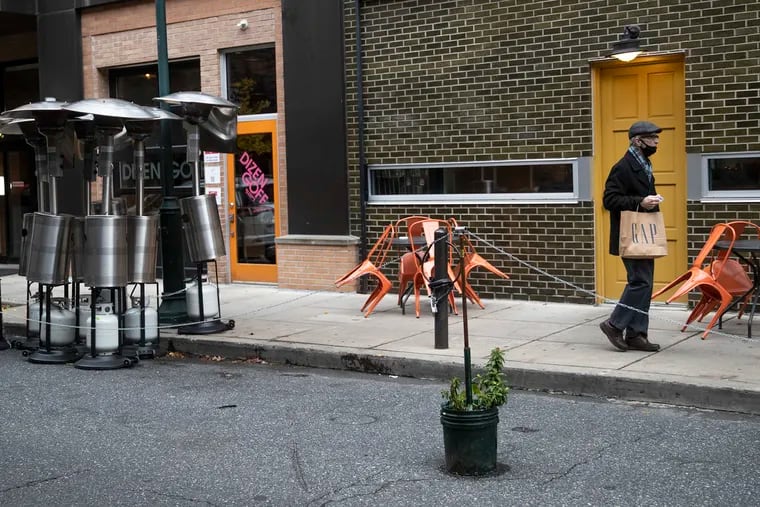 A masked pedestrian walks past heaters and an outdoor dining setup by 16th and Sansom Streets in Philadelphia. Restaurants are no longer allowed to host indoor dining due to the latest coronavirus restrictions as cases in the region surge.