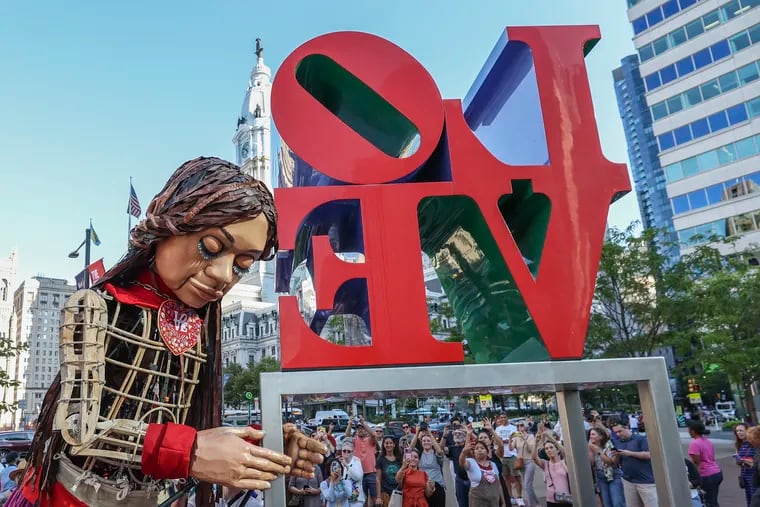 Little Amal rests her head on the Love sign at Love Park.