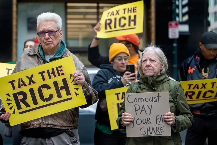 People hold signs during a rally outside the Comcast Center in Philadelphia on tax day, April 18, 2022.
