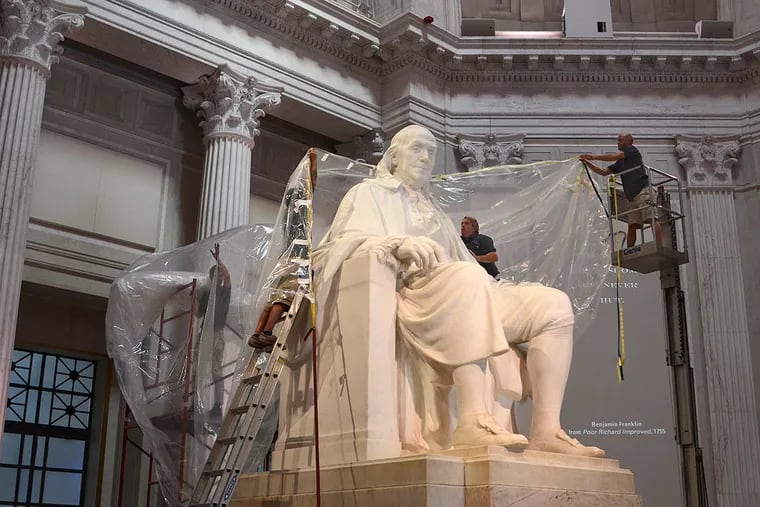 Workers from Atelier Art Services prepare to lift a special protective polyethylene covering over the iconic 20-foot high statue of Benjamin Franklin at the Franklin Institute.