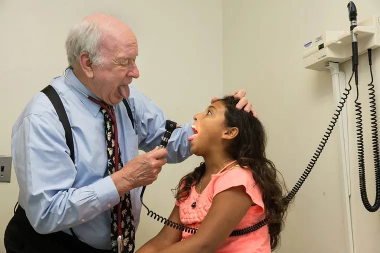 William Sharrar, 76, examines 11-year-old patient Brenda Isabela Romero at Cooper Health in Camden.