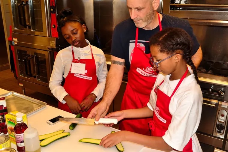 Amber Wiggins (left) and Bethany Swan get a quick lesson from chef Marc Vetri on how to score a zucchini for grilling. Vetri helped instruct "My Daughter's Kitchen" cooking class at the Free Library of Philadelphia, and taught a kitchen good-luck trick involving flying salt. (C.F. SANCHEZ / Staff Photographer)