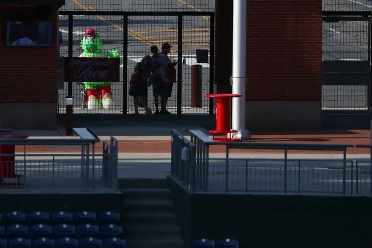 Fans who call themselves the Phandemic Krew watch from behind the gate that leads into Ashburn Alley during the first game of the Phillies' doubleheader with the New York Yankees Monday afternoon.