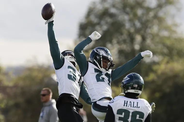 Eagles cornerback Jalen Mills (left) reaches for the football past cornerback Ronald Darby (center) as defensive back Deiondre' Hall watches before the start of practice at the London Irish training ground in Southwest London on Friday.