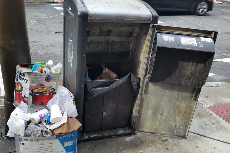 A BigBelly trash compactor at 12th and Locust with a broken door and trash piled beside it.