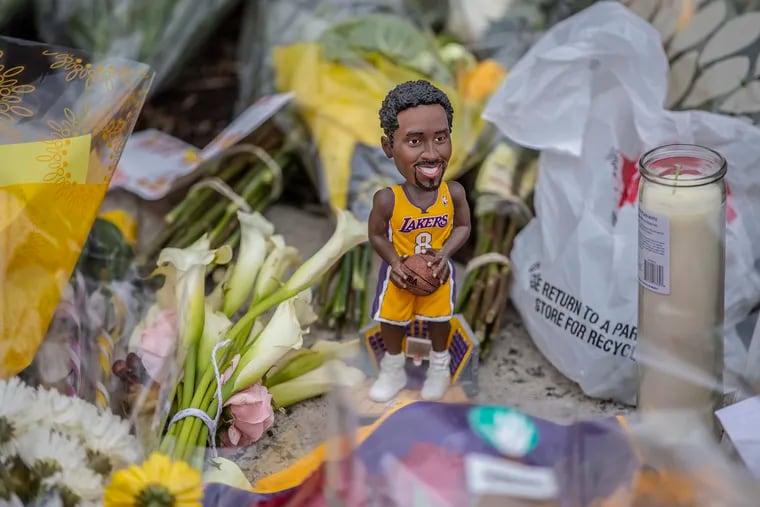 A Kobe Bryant bobblehead doll sits among the flowers in the Kobe Bryant memorial that has grown in front of Bryant Gymnasium at Lower Merion High School on January 28, 2020.