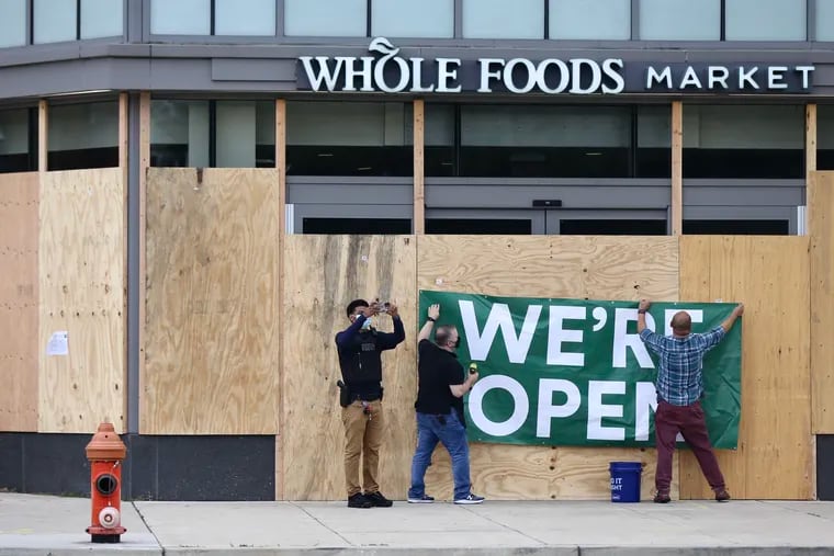 Whole Foods workers board up an entrance but hang a sign saying “WE’RE OPEN” near the homeless encampment on the Benjamin Franklin Parkway in Philadelphia on Sept. 9, 2020. Camp residents left the encampment this week but the Whole Foods chain is struggling, analysts say. Wednesday.