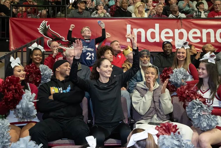 Basketball great Sue Bird (center) flaps her arms as it was announced that she was inside the St. Joseph's Hawk mascot costume during the first half against Loyola (Md.) on Friday at Hagan Arena. St. Joseph's greats Jameer Nelson (left) and Natasha Cloud are beside her.