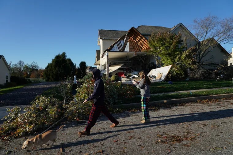 Nearby neighbors Shane wilson, left, and sister Noelle Wilson, center, walk their dog Auggie past a damaged house on Chelsea Court in Thornbury Township.