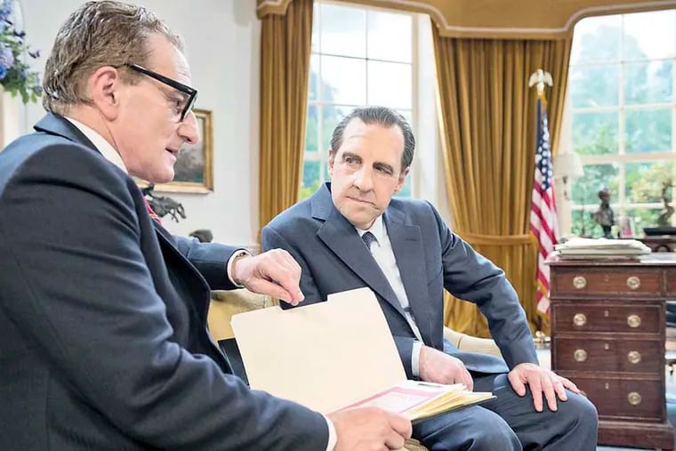 Henry Goodman as  Henry Kissinger with folder and Harry Shearer as Nixon sitting.
Photo Credit: Justin Downing